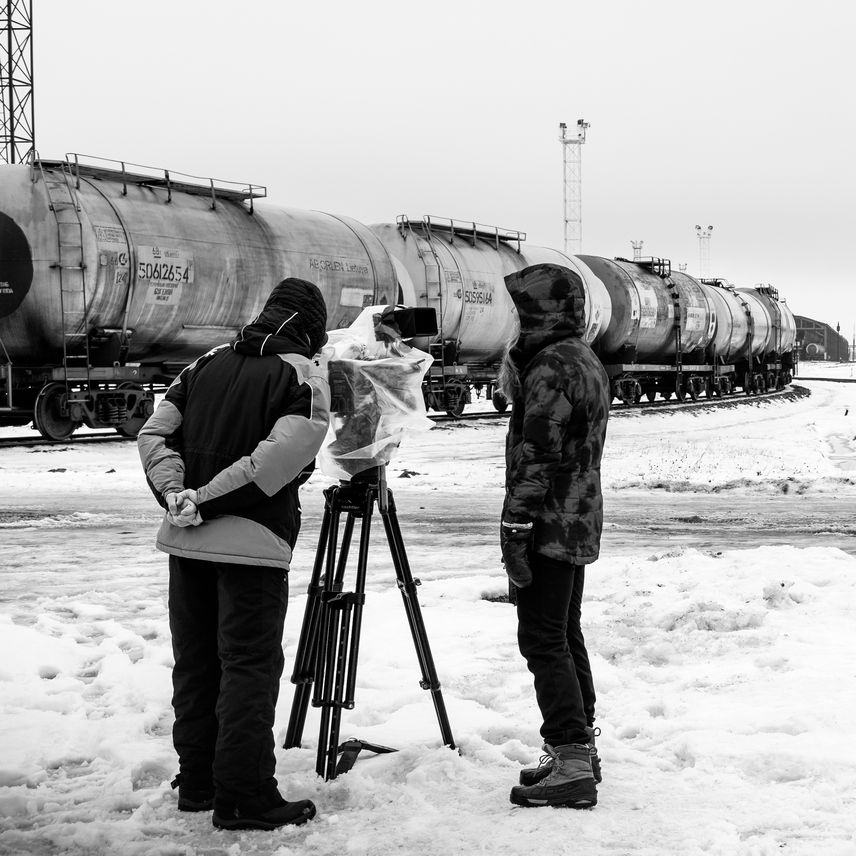 Operator i reżyserka stoją przy kamerze. Na drugim planie jedzie pociąg towarowy.
