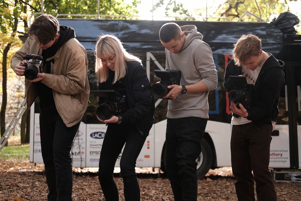 Czterech usmieczhniętych młodych ludzi stoi przez Cinebusem trzymając kamery